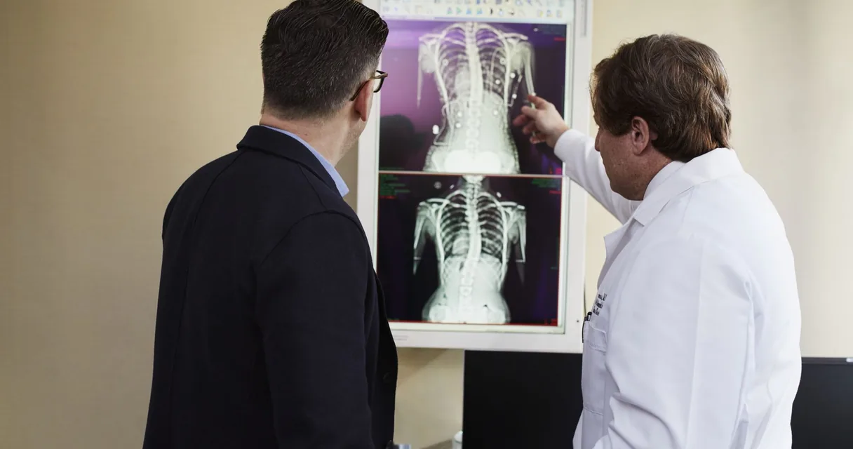 Médico apontando o resultado de uma radiografia no negatoscópio para um paciente de terno
